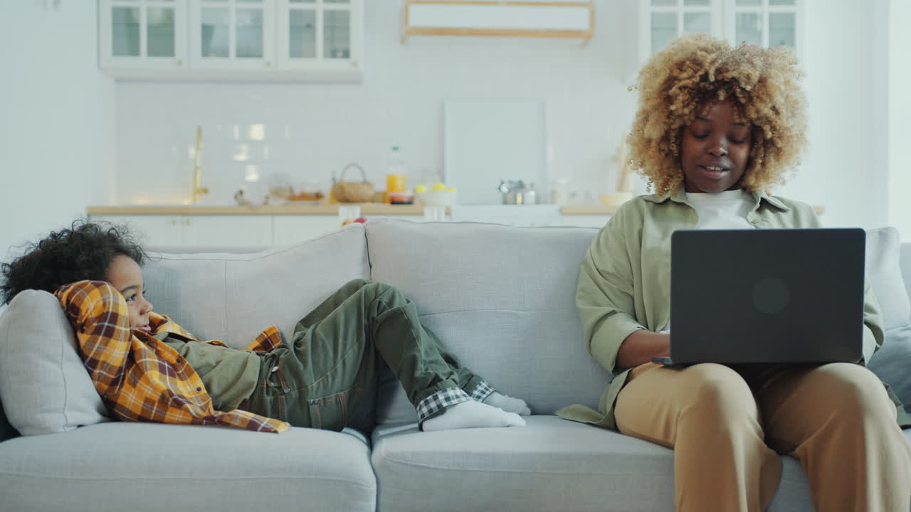 African American Mom Using Laptop and Talking to Little Son at Home