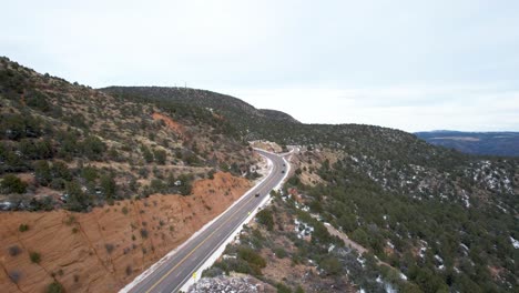 high desert road up mountain pass with pine trees, light snow and red cliffs