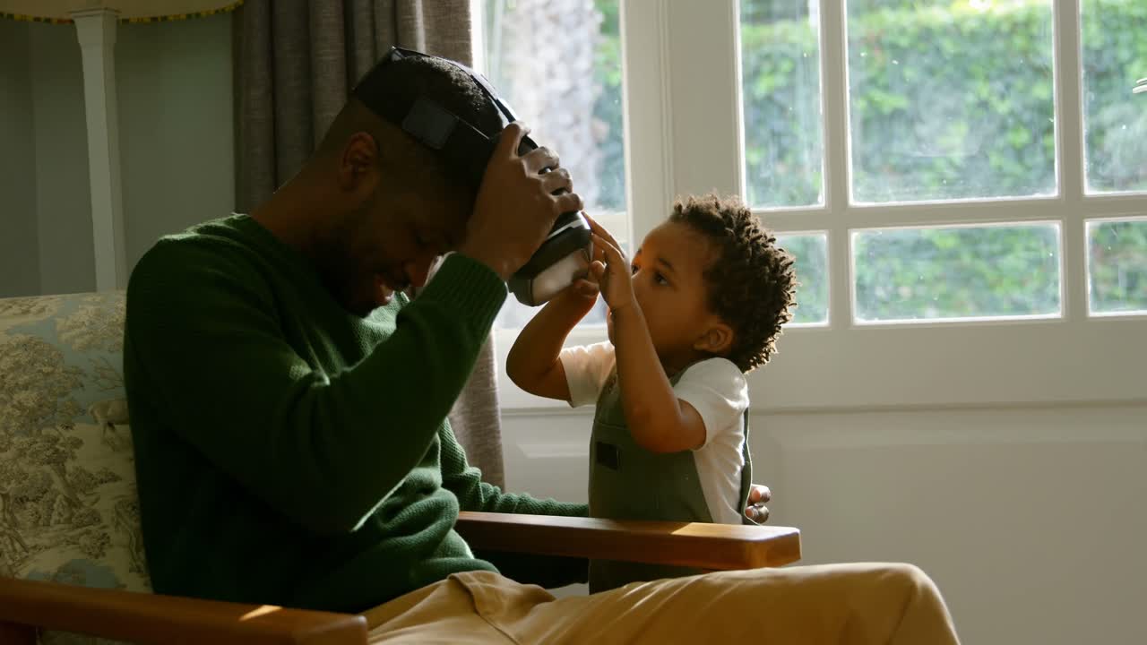 Side view of little black son removing virtual reality headset from father in a comfortable home 4k
