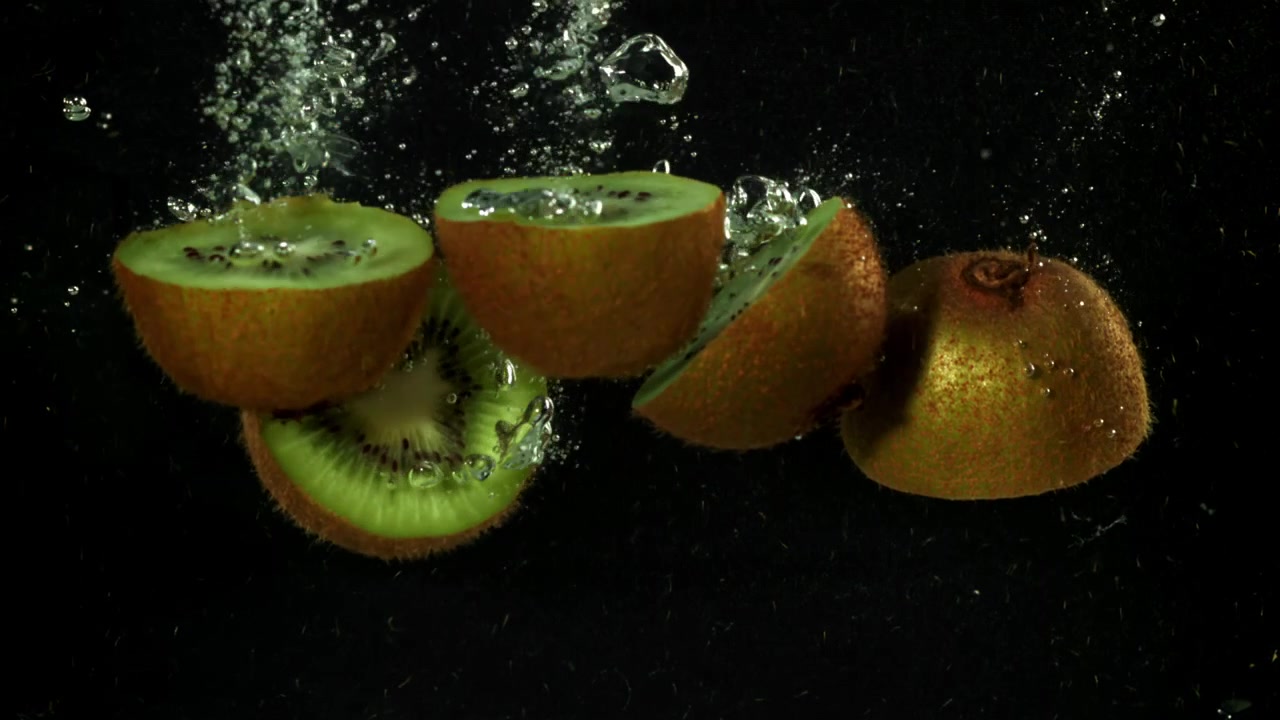 Mitades de kiwi fresco cayendo al agua en cámara lenta.