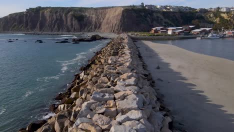 Aerial-dolly-rock-wall-jetty-separating-large-sandbank-and-ocean-wave