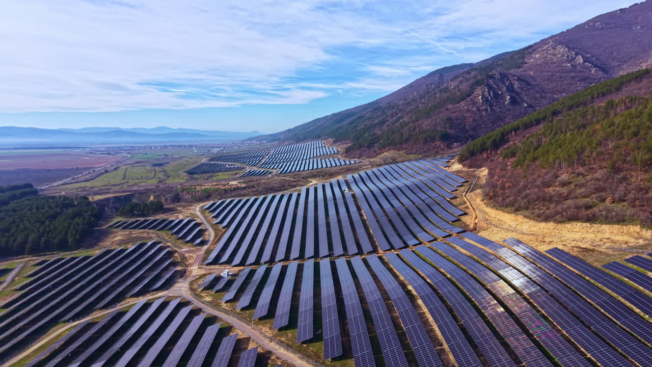 Solpaneler dækker et stort område i et vedvarende energiprojekt nær bjerge under en klar himmel.