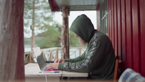 young man hoodie working on laptop computer outside his cabin