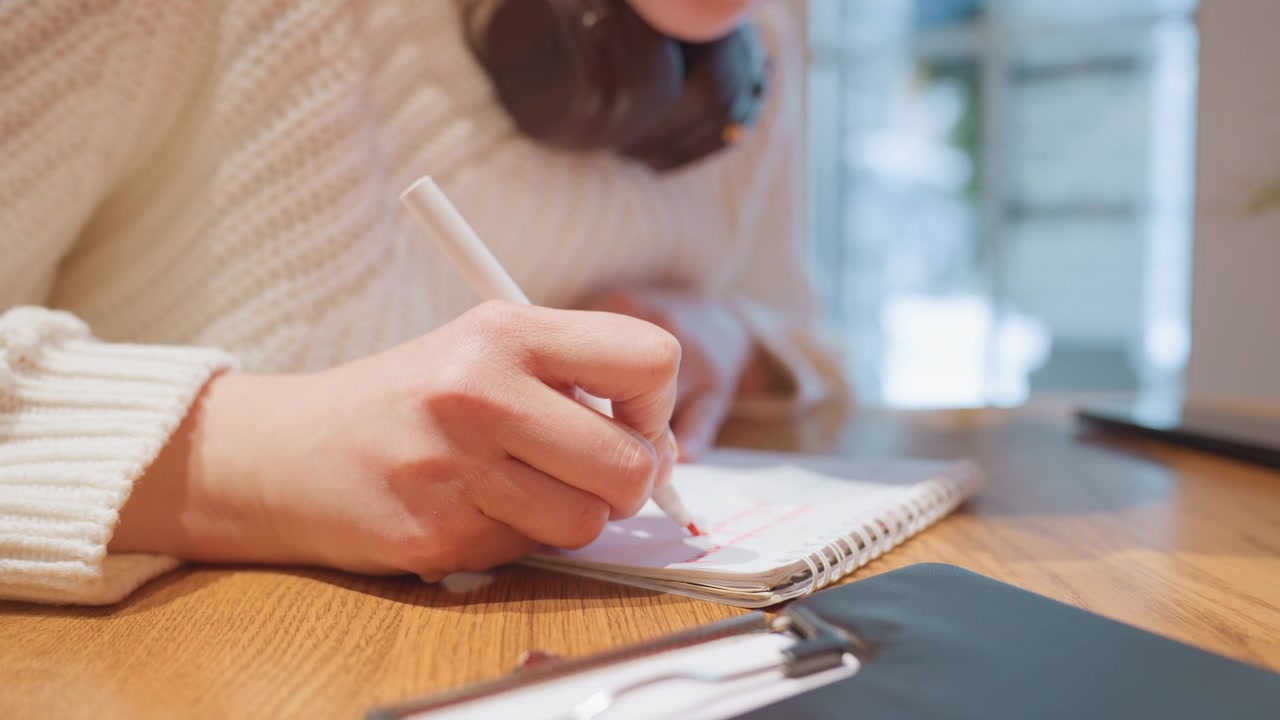 Close-up of a Person Writing in a Notebook with a Red Marker