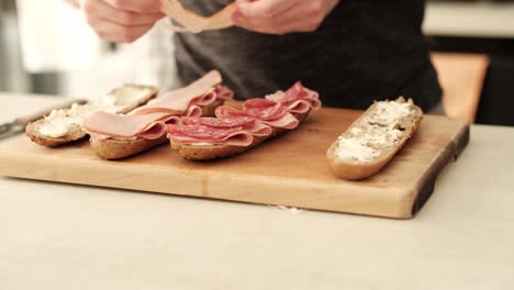 caucasian male placing sliced turkey ham on a halved brown baguette in the kitchen on the countertop