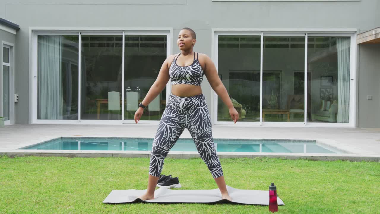 feliz mujer afroamericana de talla grande practicando yoga, de pie estirándose en el jardín