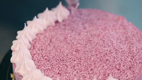 confectioner decorates top of pink cake using pastry bag