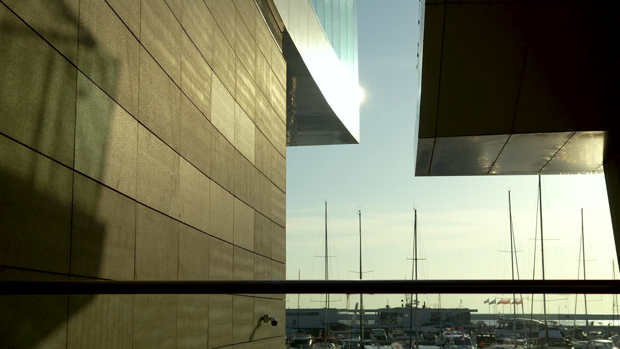 edificio moderno con vidrio y piedra cerca de una marina con mástiles de veleros en el fondo