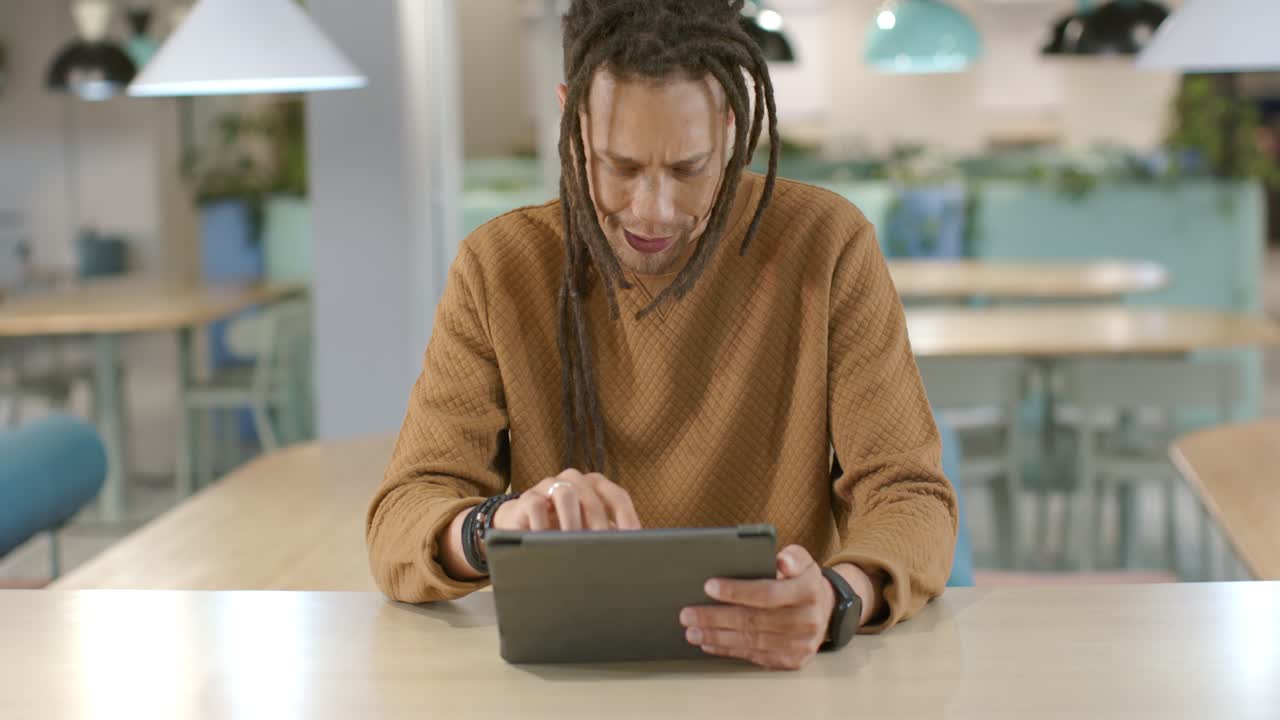 African American man steadying tablet with left hand in cafe, tapping and scrolling for work