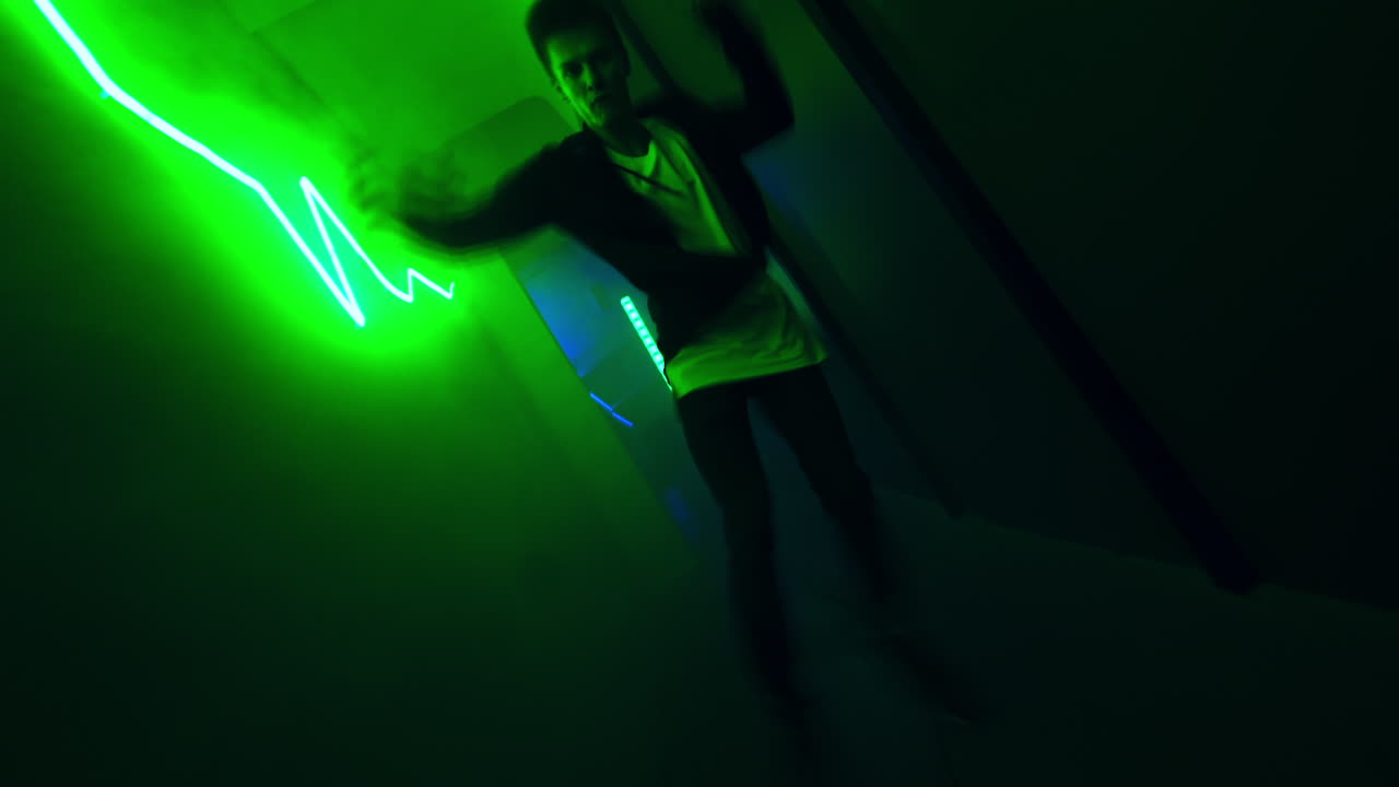 Young man dances in the long narrow corridor. Hip hop dancer performs in the green light hall.