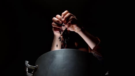 manos de un cocinero que vierte frijoles en una gran olla de metal a la luz de un fondo oscuro