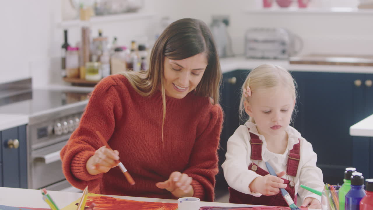 madre con hija en casa haciendo artesanía y pintando cuadros en la cocina