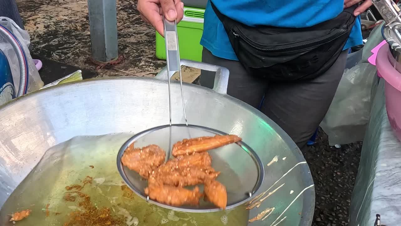 Close-up of chicken wings being fried in hot oil using a metal strainer.