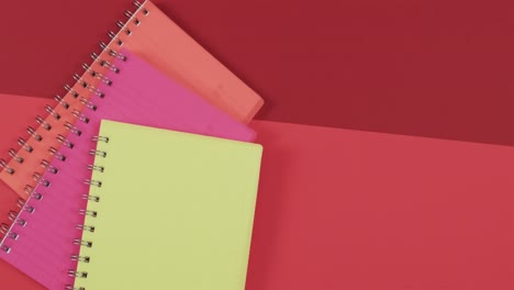Overhead-view-of-colourful-notebooks-with-copy-space-on-red-background,-in-slow-motion