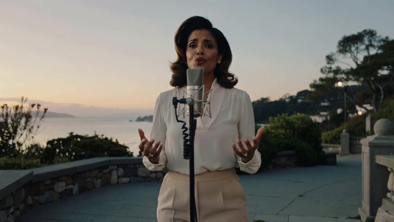 Donna che canta in camicetta bianca e pantaloni beige al tramonto, si gira verso la telecamera e registra con il microfono.