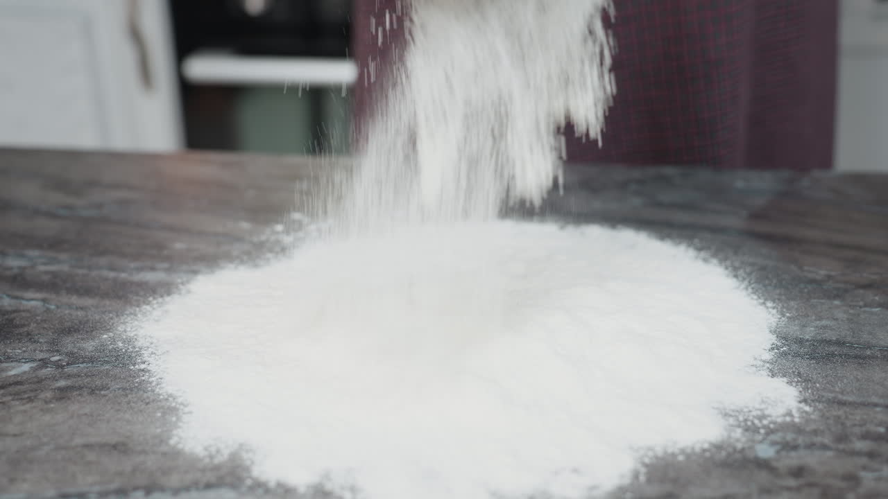 밀가루는 깨한 카운터에 여 부드럽고 가루 모양의 층을 만들어 가정 주방 환경에서 베이킹 준비, 질감 및 음식 프로세스를 강조합니다.