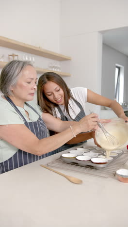 vertical video: baking cupcakes together, grandmother and granddaughter pouring batter into molds