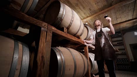 authentic shot of successful male sommelier is tasting a flavor and checking white wine quality poured in transparent glass in a wine cellar.