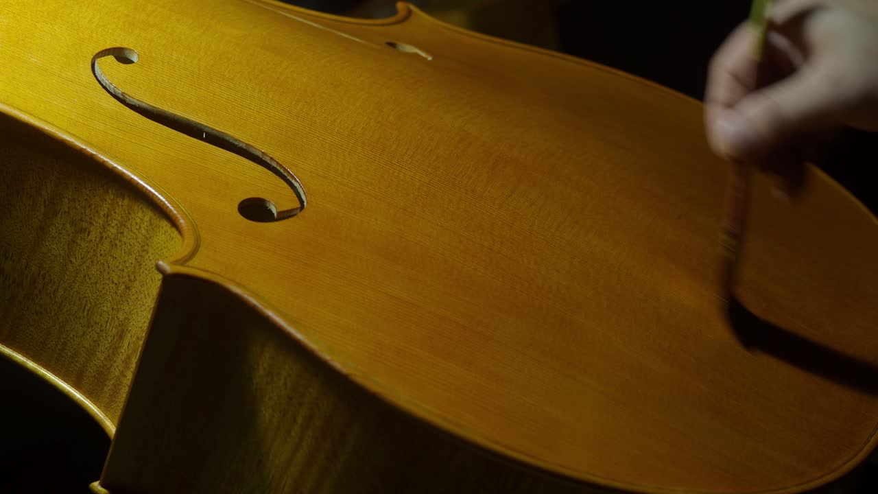 Skilled luthier applying varnish on cello top plate with self made alcohol varnish, highlighting intricate woodworking process in traditional instrument crafting
