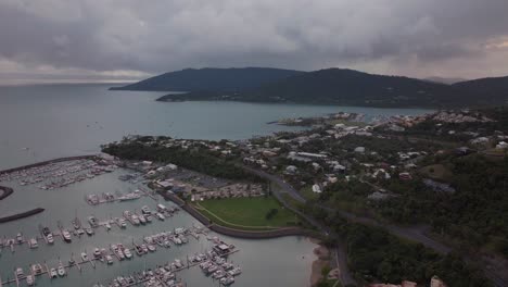 Port-Airlie-Beach-Bay-Lagoon-Coral-Sea-marina-aerial-drone-sunrise-morning-heart-of-Great-Barrier-Reef-Whitsundays-Whitehaven-jetty-yachts-sailboats-buildings-backwards-reveal-motion