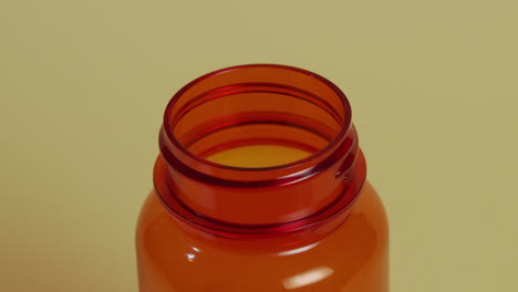 Slow-motion-high-angle-close-up-of-a-pill-bottle-as-a-single-pill-falls,-hits-the-rim-and-bounces-in