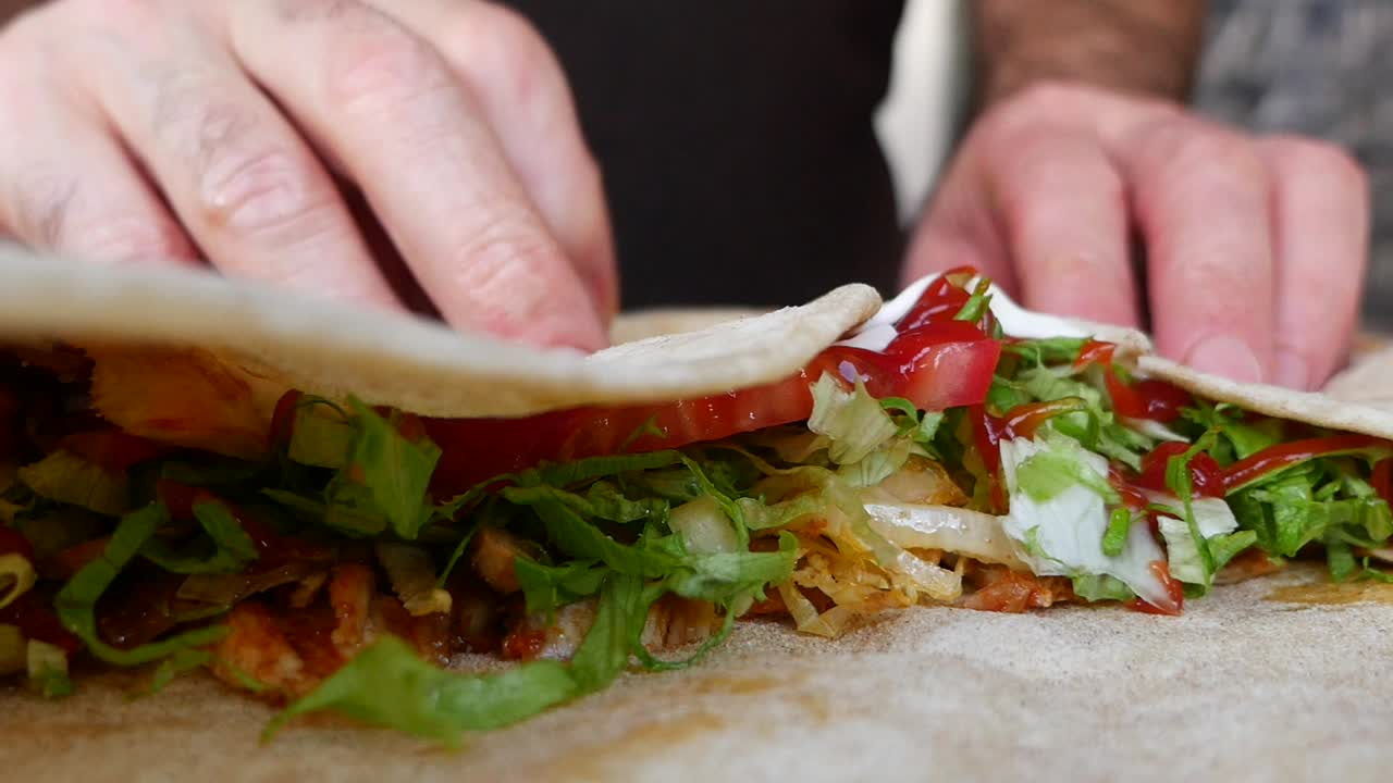 Primo piano di mani che arrotolano un delizioso shawarma di pollo