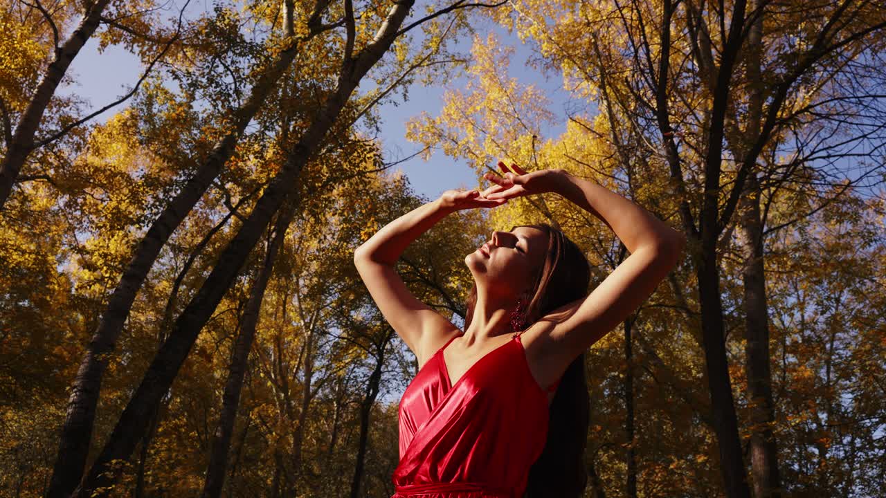 Embracing Nature's Beauty: A Dance of Freedom in a Vibrant Red Dress Against a Backdrop of Autumn Leaves and Sunlit Trees
