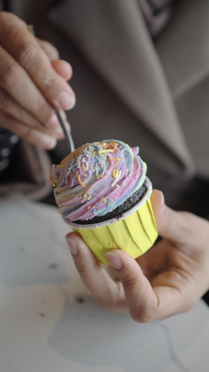 Persona che mangia un cupcake colorato glassato con un cucchiaio