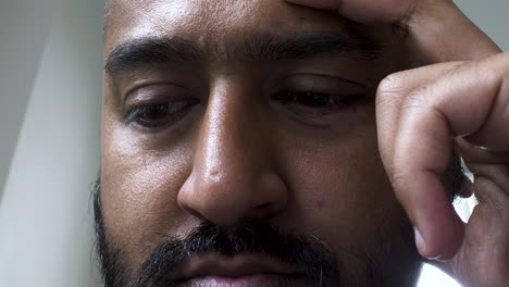 An-extreme-close-up-shot-cropped-on-the-eyes-of-an-Asian-Indian-man-concentrating-and-focused-on-work-with-his-fingers-resting-on-the-side-of-his-head