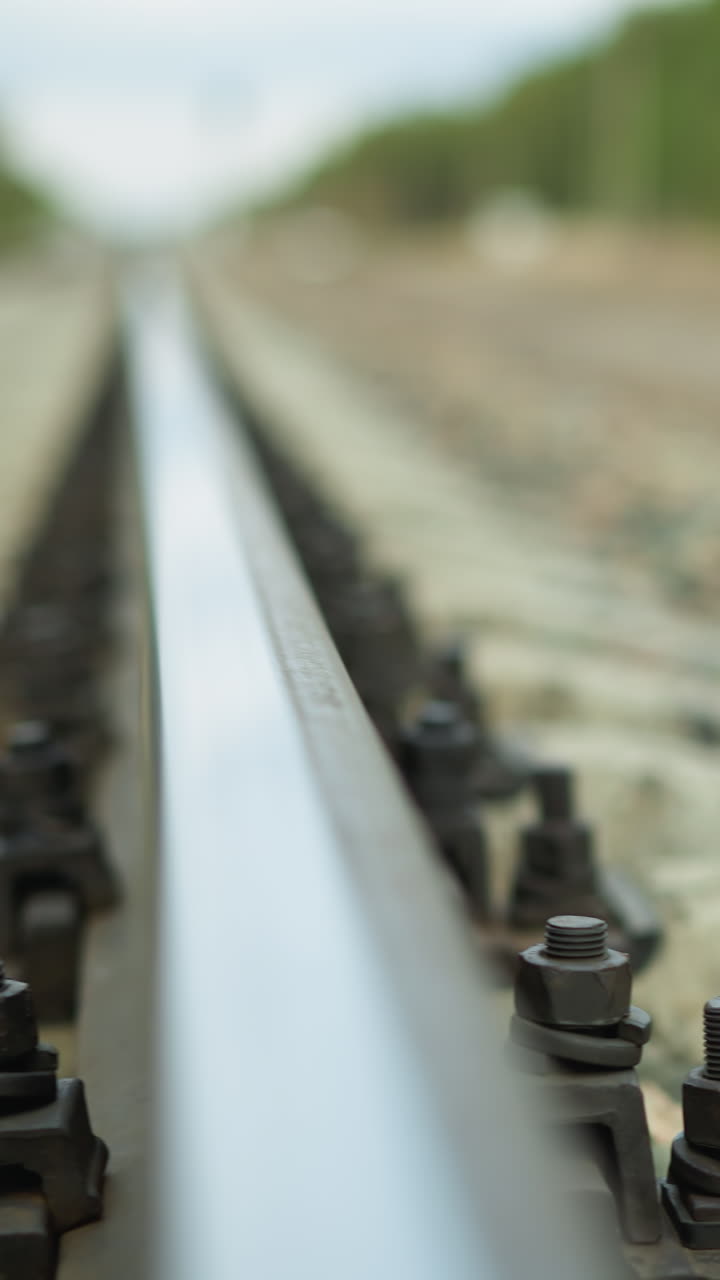 близкий вид камеры, уходящей от железнодорожного пути, простирающегося на расстояние, съемка сосредоточена на рельсе и его креплениях, с красиво размытым фоном, с