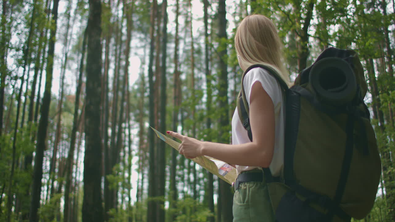 지도와 배 ⁇ 을 들고 여름 휴가 날에 자연 트레일에서 야외에서 휴식을 취하는 젊은 여성 여행자. 라이프 스타일 하이킹 개념. 숲 여행. 지도로 방향을 선택.