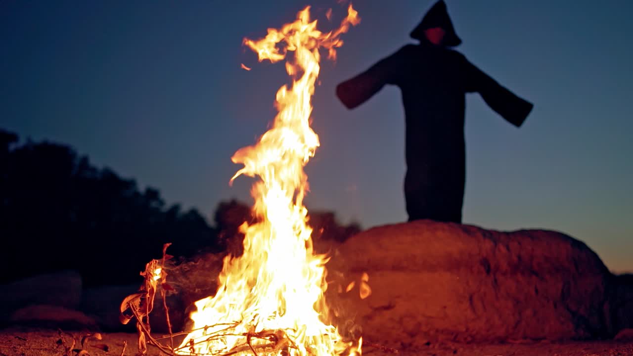Terrible witch in the forest. Witch raising hand up near fire in forest