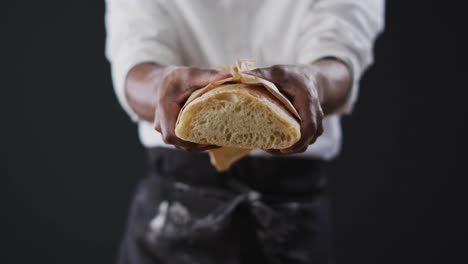 Video-of-cook-holding-loaf-of-bread-on-black-background