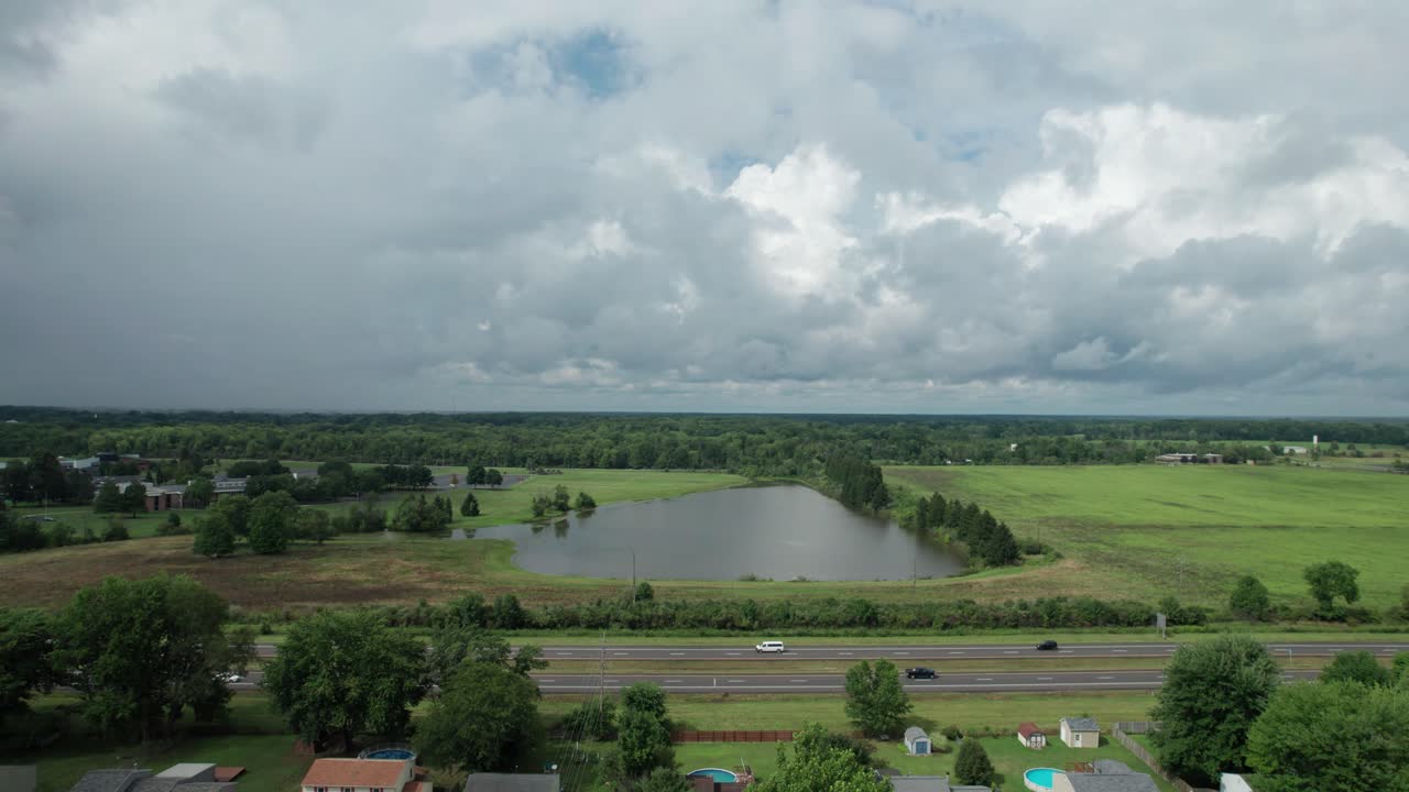 un hermoso lago tranquilo es visible desde un dron que se cierne sobre una carretera transitada con vehículos en movimiento