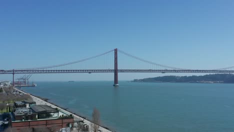 aerial drone shot over the tagus river with the 25th of april bridge in the background in lisbon, portugal