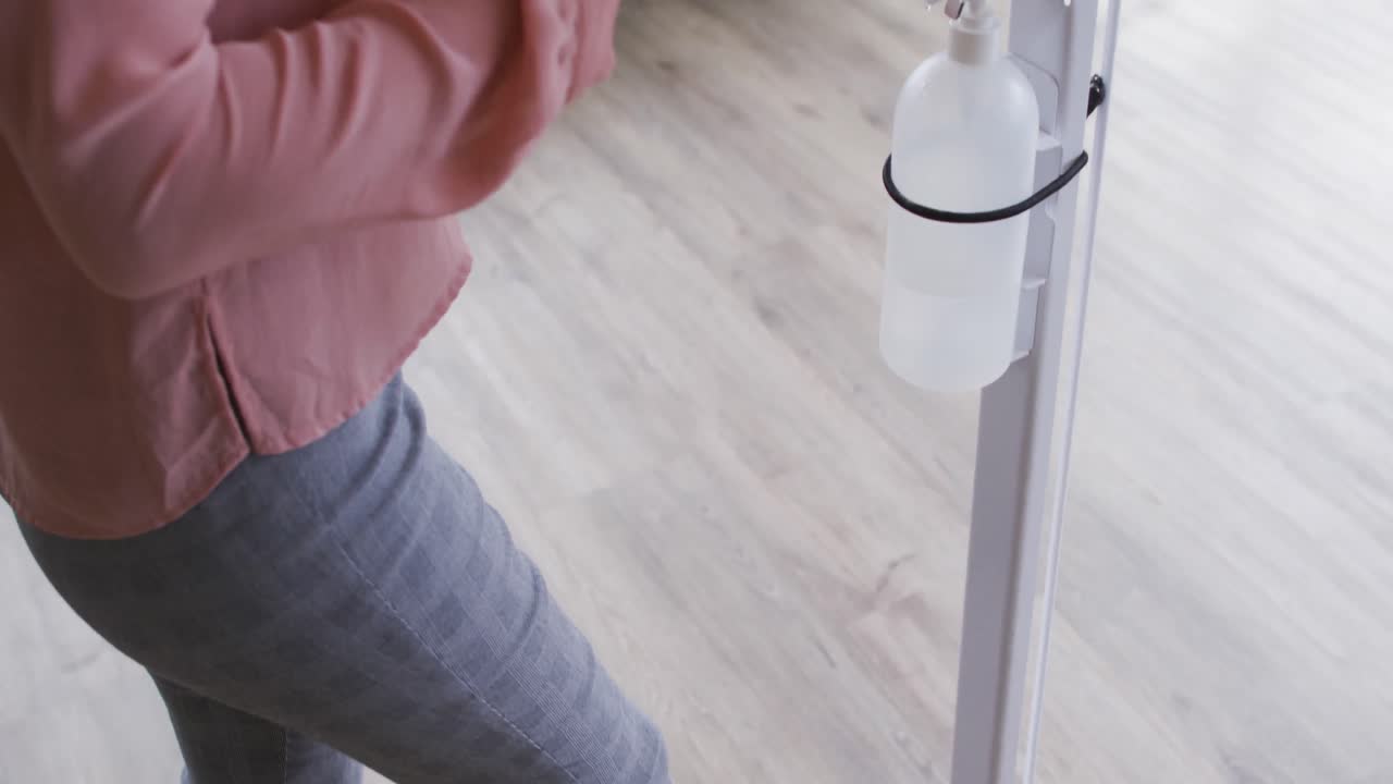 사업가 여성 이 작업장 에 들어갈 때 손 을 소독 하기 위해 발  ⁇ 프 소독제 를 사용 하고 있다