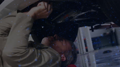 male mechanic lying under car inspecting undercarriage in auto repair, with floating blue overlay