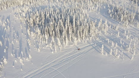 drone shot of a man riding a snowmobile on track path through winter forest in sweden