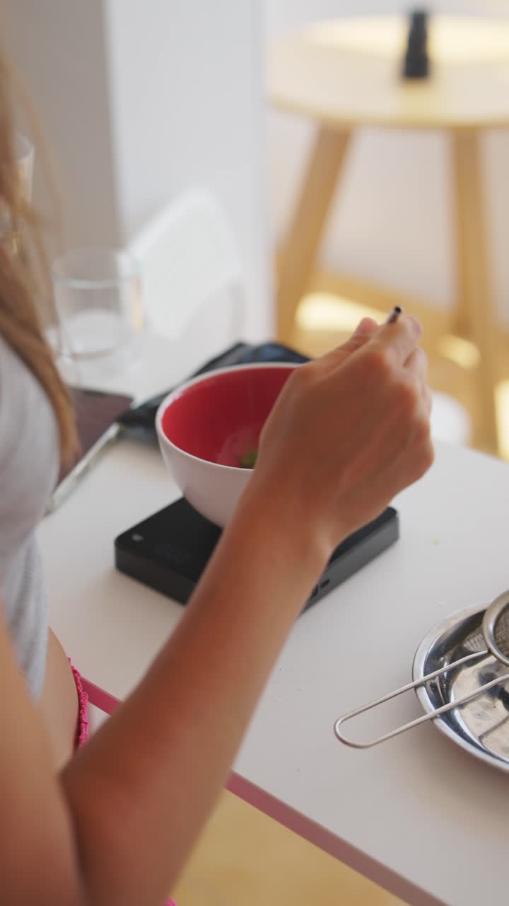 Hands preparing a drink, pouring water into a bowl of matcha powder on a kitchen scale