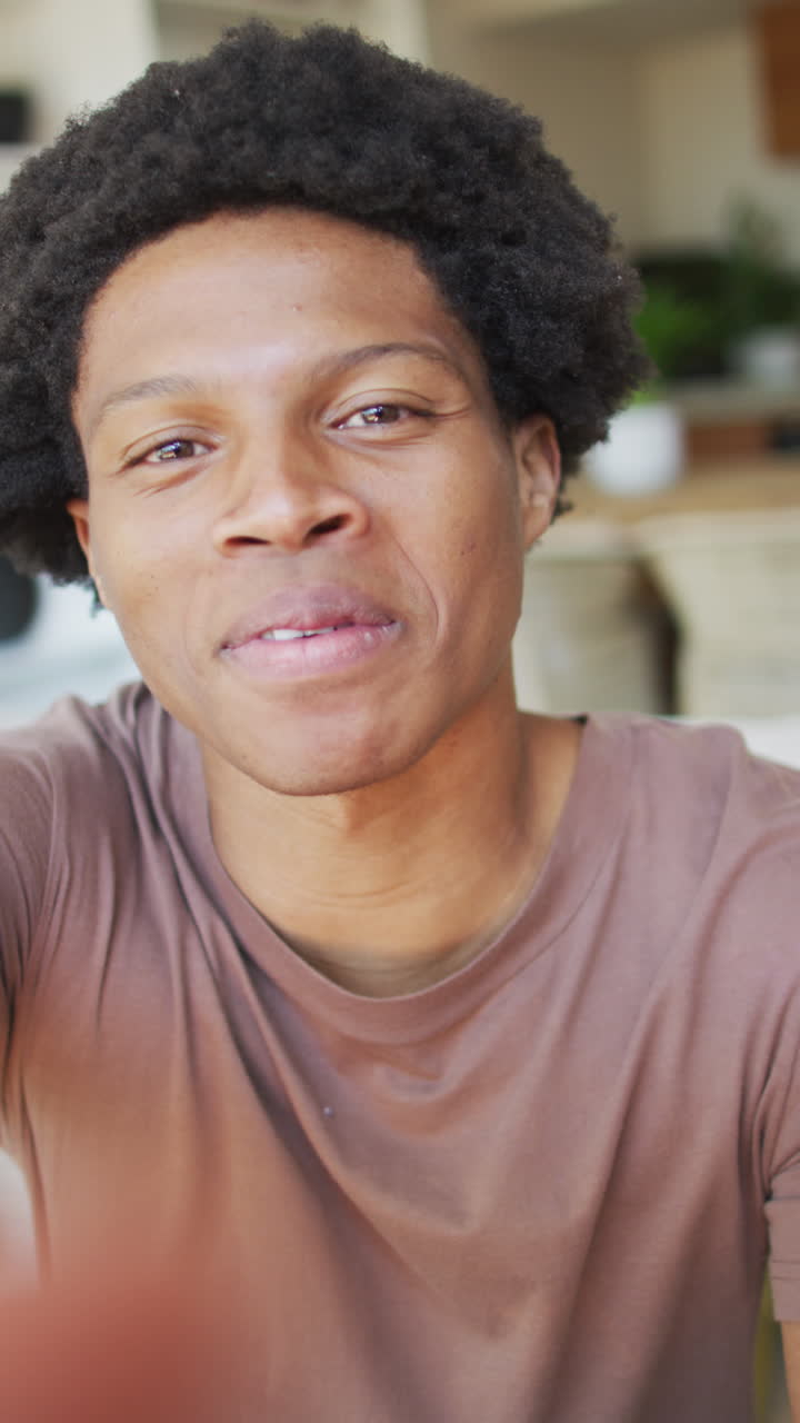 video vertical de un feliz hombre afroamericano haciendo una llamada de video, hablando y soplando besos