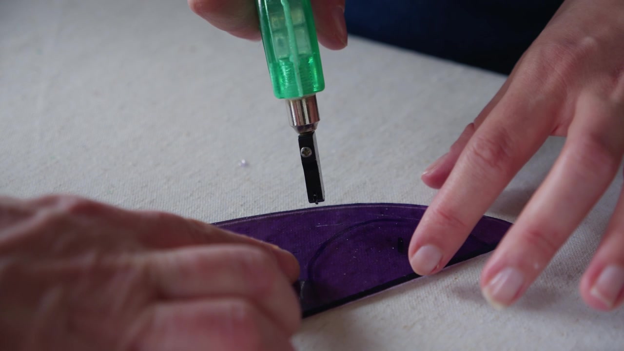 A teacher shows her female student how to score a piece of purple stained glass during an art class at a luxury hotel.