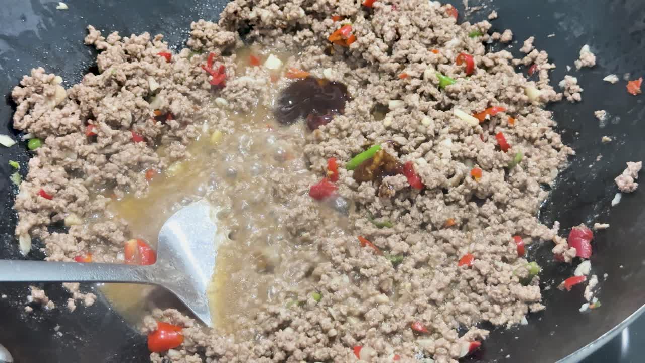 Ground pork, chili, and sauce are vigorously stir-fried in a hot wok under bright lighting, with dynamic utensil movement and close-up framing