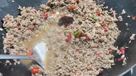 ground pork, chili, and sauce are vigorously stir-fried in a hot wok under bright lighting, with dynamic utensil movement and close-up framing