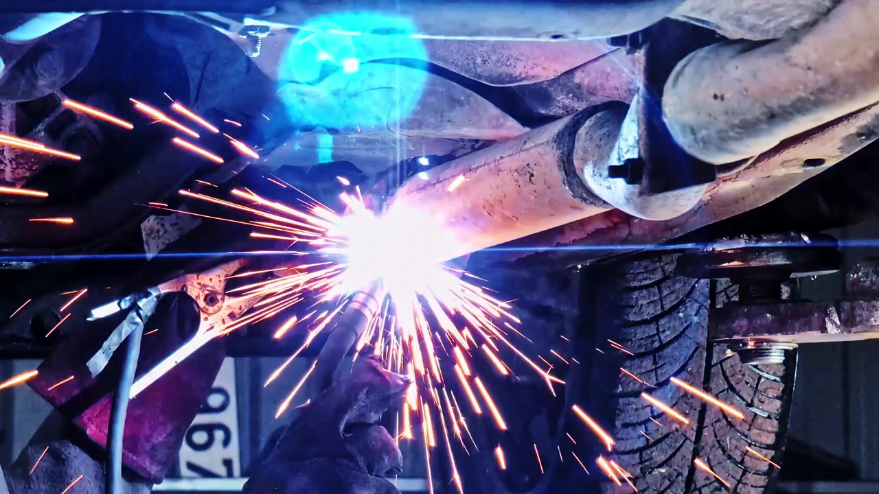 Mechanic performing repairs on a vehicle exhaust system welding a damaged section
