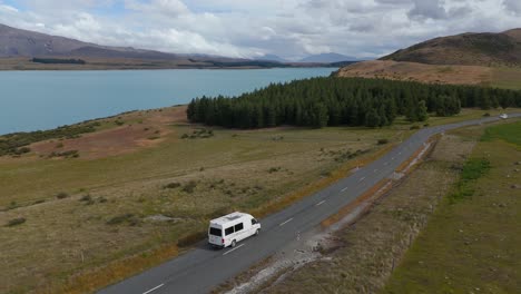 Aerial-view-of-a-camper-driving-on-a-road-next-to-lake-Tekapo