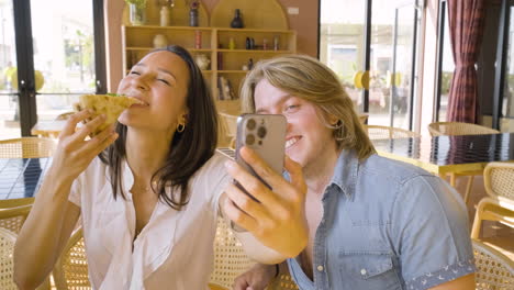 Niña-Feliz-Comiendo-Pizza-Y-Tomando-Una-Foto-Selfie-Con-Su-Amigo-En-Un-Restaurante