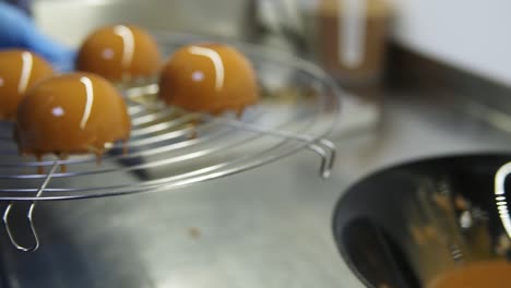 Unrecognizable-confectioner-hands-in-blue-gloves-take-a-tray-with-glazed-cakes-away-to-finish-the-preparation-of-delicious-desserts.