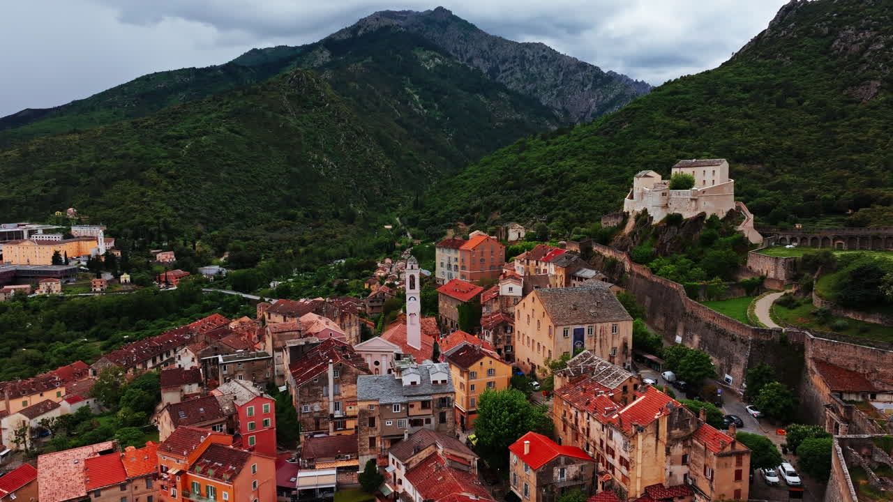 Aerial drone shot over the historic town of Corte, Corsica, France. High view of the old town and fortress overlooking the landmark on top of the hill. View of the scenic landscape and mountains