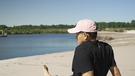 un joven masculino hispano está sentado solo junto a un hermoso lago, admirando la vista