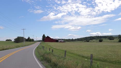 driving down country road with barb wire fence towards red barn on farm with electric wires by side of road cinematic hd